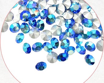 May include: A collection of iridescent blue and silver rhinestones, scattered across a white background. The rhinestones vary in size and shape, reflecting light with a sparkling effect. Ideal for crafting or embellishing projects.