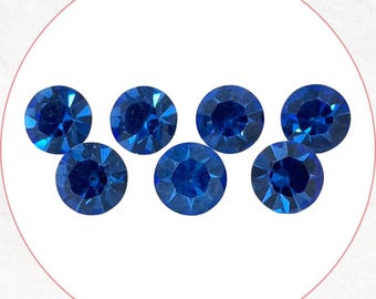 May include: Seven round, faceted, deep blue gemstones arranged in a semi-circle. The gems are set against a white background, enclosed within a pink circle. The facets catch the light, creating a sparkling effect. Ideal for jewelry making or craft projects.