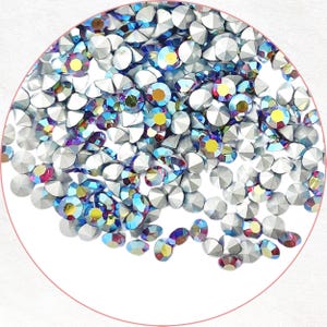 以下が含まれることがあります： シルバーベースとカラフルな輝きを持つ、イリデッセントラインストーンのコレクション。ラインストーンはファセットカットで、青、黄色、紫の色合いで光を反射します。これらの装飾用宝石は、ネイルアートや工芸品に最適です。