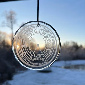 Può includere: Un ornamento di vetro trasparente con un design a forma di bussola. L'ornamento presenta le parole "Stand By Stop Stand By", "Dead Slow", "Half Full", "Full", "SUNY Maritime", "Throggs Neck, NY", e "Half Full".