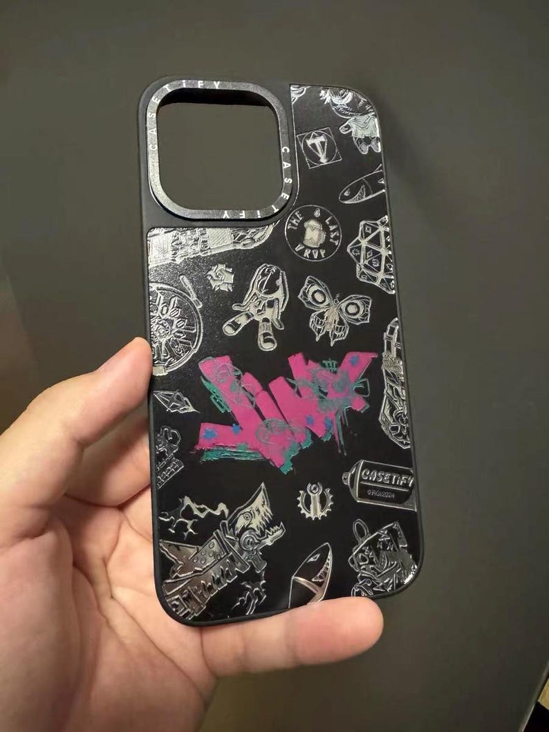 Peut inclure: Coque de t&eacute;l&eacute;phone noire avec un design graphique argent&eacute; et blanc mettant en vedette le mot "LWYK" en graffiti rose et bleu et d'autres motifs vari&eacute;s. La coque a un anneau de cam&eacute;ra sur&eacute;lev&eacute; et le texte "CASETIFY" imprim&eacute; en bas &agrave; droite.