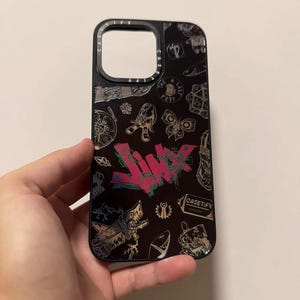 Peut inclure: Coque de t&eacute;l&eacute;phone noire avec un imprim&eacute; graphique color&eacute; repr&eacute;sentant un loup, un requin, un papillon et le texte "CASETIFY".