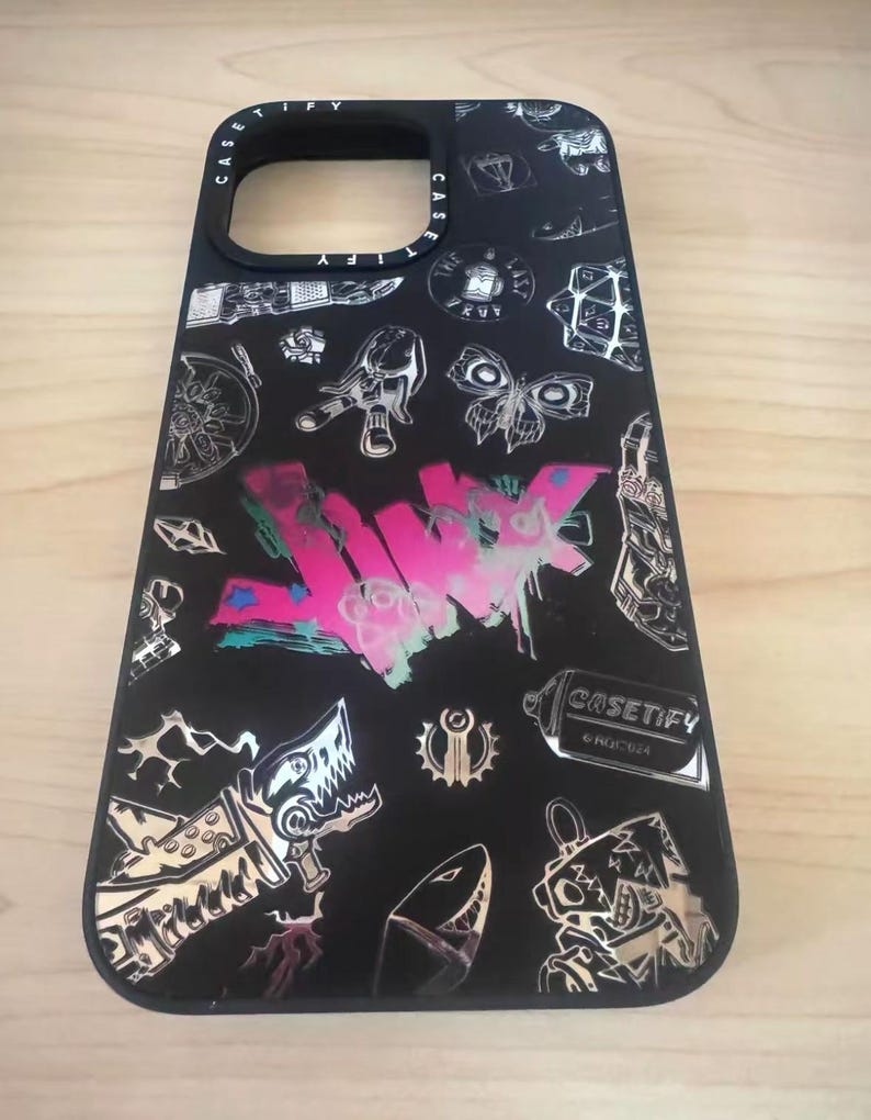 Peut inclure: Coque de t&eacute;l&eacute;phone noire avec un design graphique argent&eacute; et rose. Le design pr&eacute;sente un requin, un papillon et le mot "JUNK" en lettres roses et blanches. La coque porte &eacute;galement le texte "CASETIFY" en lettres blanches.