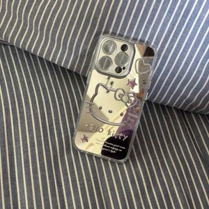 May include: A clear phone case with a mirrored back featuring a Hello Kitty design. The case has a cutout for the camera lens and a pink heart on the back. The text "Hello Kitty" is printed on the case, along with the phrase "Because your smile is the most beautiful thing in the world."