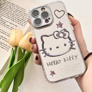 May include: Clear phone case with a Hello Kitty design. The case has a silver outline of Hello Kitty with a pink bow and a pink star. The case also has a silver heart and two silver stars.