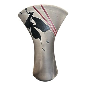 May include: A fan-shaped ceramic vase with a matte grey finish. The surface features a painted design of black abstract leaf-like shapes and two thin, parallel dark red lines that extend from the top rim down toward the center of the body.