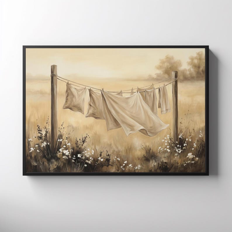 May include: A framed wall art print depicting a sepia-toned landscape with laundry hanging on a clothesline between two wooden posts. The scene features light-colored fabric sheets blowing in the wind, set against a field of tall grass and flowers.