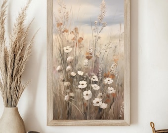 May include: A framed art print featuring a field of wildflowers in soft, muted tones. The artwork showcases white flowers, tall grasses, and hints of orange and brown, set against a light blue sky. The frame is a light wood color, adding to the piece's natural aesthetic.