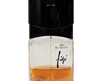 May include: A clear glass perfume bottle with a black rectangular cap. The bottle contains an amber-colored liquid. The text on the front reads Eau de Toilette, Fidji, and Parfums Guy Laroche Paris in black lettering against the clear glass surface.