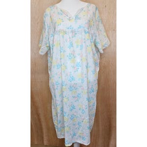 May include: A white, short-sleeved nightgown with a floral pattern in pastel yellow, blue, and pink. The nightgown has a V-neckline and a ruffled detail at the chest. The fabric appears lightweight and flowing, suitable for sleepwear.