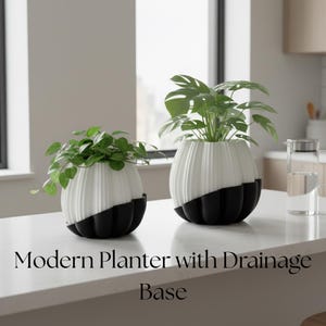 May include: Two modern planters with drainage bases. The planters are white with black bases and contain green plants. The text "Modern Planter with Drainage Base" is displayed below the planters.