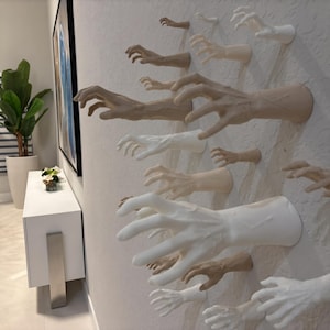 Può includere: Una collezione di molteplici sculture di mani montate a parete in varie tonalità di bianco, beige e marrone chiaro. Ogni mano è posizionata in un gesto di presa, estendendosi verso l'esterno con dettagli visibili delle dita e delle nocche.