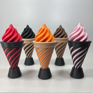 May include: A collection of colorful ice cream cone sculptures. Each cone features a different colored swirl of ice cream, including red, black, orange, brown, and pink. The cones have a black base and a striped design.