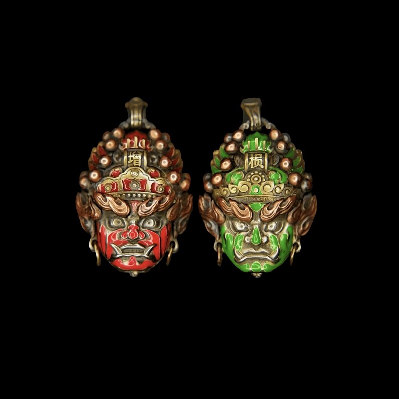 May include: Two ornate pendants featuring stylized faces with intricate details. One is red with gold accents, the other green. Both have a loop at the top for hanging and are set against a black background.