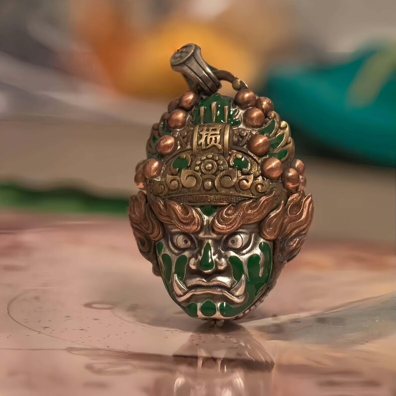 May include: A detailed pendant featuring a green and silver face with intricate gold and bronze accents. The pendant has a loop at the top for a chain and is likely a piece of jewelry or a decorative item.