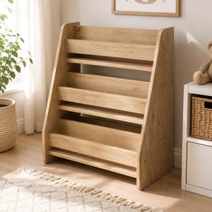 May include: A light brown wooden bookshelf featuring three horizontal tiers with front-facing ledges designed to hold books upright. The unit has a slanted side profile and a natural wood grain finish, providing an open storage display structure.