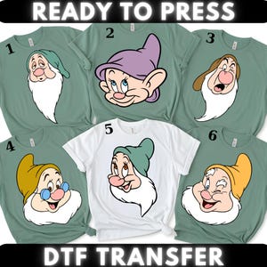 以下が含まれることがあります： 6枚のTシャツのコレクション。漫画の小人キャラクターが特徴です。シャツは緑と白など、さまざまな色があります。各シャツには、ユニークな表情の異なる小人キャラクターが表示されます。「READY TO PRESS」と「DTF TRANSFER」の文字が上部と下部にあります。