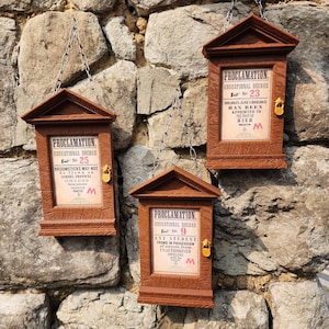 May include: Three brown wooden wall-mounted display frames with triangular pediments and metal hanging chains. Each frame contains a printed proclamation labelled Educational Decree No. 25, No. 9, and No. 23, featuring a small gold-coloured padlock.