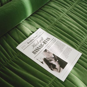 May include: A mock newspaper announcement with the headline "Hochzeit Hannah + Ryan" and a black and white photo of a couple kissing. The announcement is on a green velvet surface.