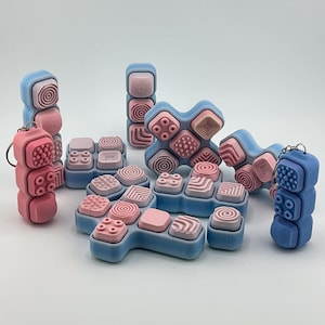 Puede incluir: Colección de juguetes sensoriales azules y rosas con diversas superficies texturizadas. Los juguetes están dispuestos en diferentes configuraciones, incluyendo pilas y formas conectadas. Algunos tienen llaveros.