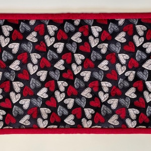 May include: A red and white table runner with a black background and a pattern of hearts. The runner has a red border.