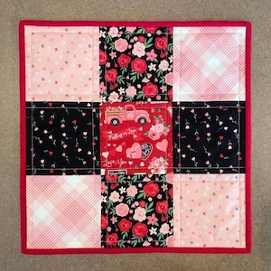 May include: A red, black, and pink patchwork quilt with a Valentine's Day theme. The center square features a red truck with the words "Falling in Love" and "Love You".