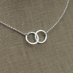 May include: A silver chain necklace with a delicate pendant featuring two interlocking circles.