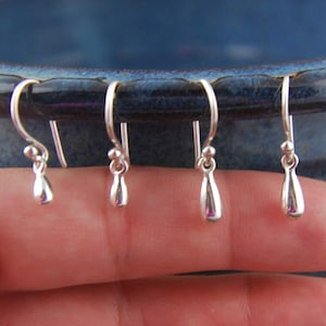 May include: Four silver teardrop-shaped earrings with a hook closure.