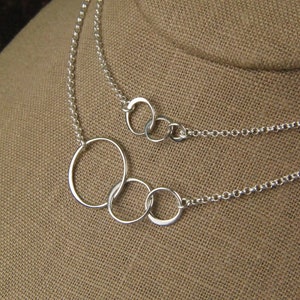 May include: A silver necklace with four interlocking circles, the largest circle is the outermost and the smallest circle is the innermost.