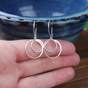 May include: A pair of silver dangle earrings with two interlocking circles. The earrings have a simple and elegant design.