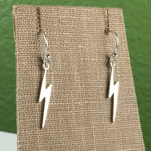 May include: A pair of silver lightning bolt earrings on a brown fabric display stand.