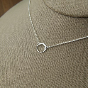 May include: A silver chain necklace with a small, simple circle pendant.