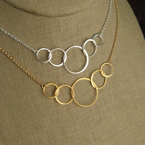 May include: Two necklaces with multiple interconnected circles. The top necklace has five silver circles and the bottom necklace has five gold circles.