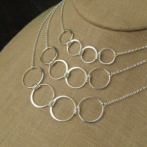 May include: A silver necklace with multiple interconnected circles of varying sizes. The circles are linked together with a twisted wire design.