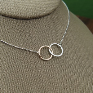May include: A silver chain necklace with two interlocked circles, one silver and one rose gold.