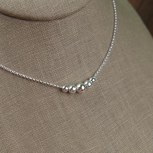 May include: A silver necklace with a graduated chain and five round silver beads.