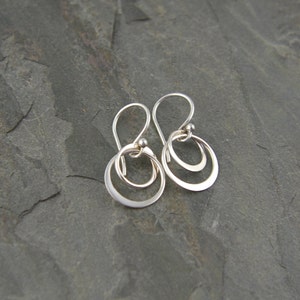 May include: A pair of silver dangle earrings with two overlapping circles. The earrings have a simple, minimalist design.