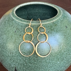 May include: Gold-toned earrings with four interlocking circles hanging from a hook.