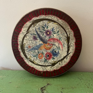 May include: Round vintage tin with a bird and floral design. The tin features a central image of a colorful bird surrounded by flowers in shades of blue, orange, and red. The rim has a red and brown striped pattern.