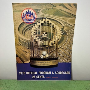 以下が含まれることがあります： 1970年のニューヨーク・メッツ・ワールド・チャンピオンシップ・トロフィーのヴィンテージプログラムとスコアカード。プログラムには、金のトロフィー、メッツのロゴ、スタジアムのシーンが描かれています。プログラムは青色の背景で、25セントです。