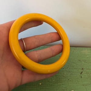 May include: A bright yellow bangle bracelet. The circular bracelet is a solid, vibrant yellow color. The smooth, glossy surface reflects light, highlighting its rounded shape. The bangle is a simple, yet eye-catching accessory.