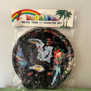 May include: A black metal tray and coaster set featuring a Florida theme. The tray and coasters have a floral border and a map of Florida with dolphins and hibiscus flowers. The packaging reads "FLORIDA METAL TRAY AND COASTER SET."