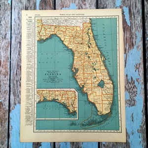 Op de afbeelding: Een vintage kaart van Florida van Rand McNally. De kaart is gedrukt op crèmekleurig papier met een blauwe rand en toont de county's en belangrijkste steden van de staat. De kaart heeft de titel "Rand McNally Popular Map of Florida" en bevat een legenda en een schaal.