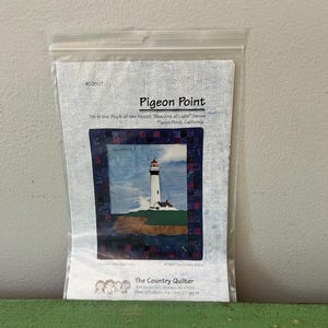 Könnte beinhalten: Eine transparente Plastiktüte mit einem Stoffpaneel mit einem Leuchtturm-Design. Das Panel trägt die Aufschrift "Pigeon Point" und gehört zur Serie "Beacons of Light". Das Logo von The Country Quilter ist sichtbar.