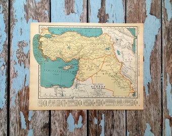 May include: A vintage map print depicting Turkey, Syria, and Iraq, with surrounding countries and seas. The map uses beige, yellow, and blue hues, showing geographical details and text. The print is on aged paper, with a detailed cartographic style.