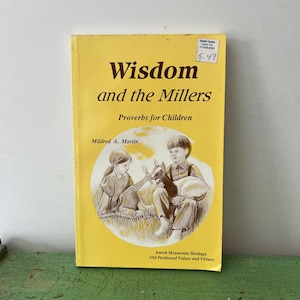 Op de afbeelding: Een geel boek met de titel "Wisdom and the Millers" met de ondertitel "Proverbs for Children". De omslag toont een illustratie van twee kinderen met een geit. De auteur is Mildred A. Martin.