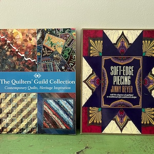 May include: Two books on a green surface. The book on the left is titled "The Quilters' Guild Collection" with the subtitle "Contemporary Quilts, Heritage Inspiration." The book on the right is titled "Soft-Edge Piecing" by Jinny Beyer.