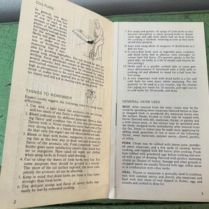 May include: Open book with pages detailing herb culture and uses. Text includes instructions for cooking with herbs, such as marjoram, thyme, and parsley. The book is open on a green surface.