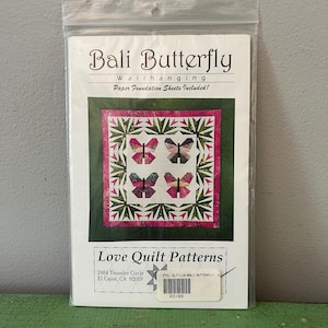 May include: A package for a Bali Butterfly wall hanging quilt pattern. The pattern features four butterfly designs in pink, green, and black. The package includes paper foundation sheets. The brand is Love Quilt Patterns.