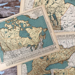 May include: Vintage maps of Canada, featuring provinces and territories in shades of beige, blue, and brown. The maps are from a Rand McNally atlas, with detailed geographical information and text. The maps are layered on a weathered, blue-toned wooden surface.